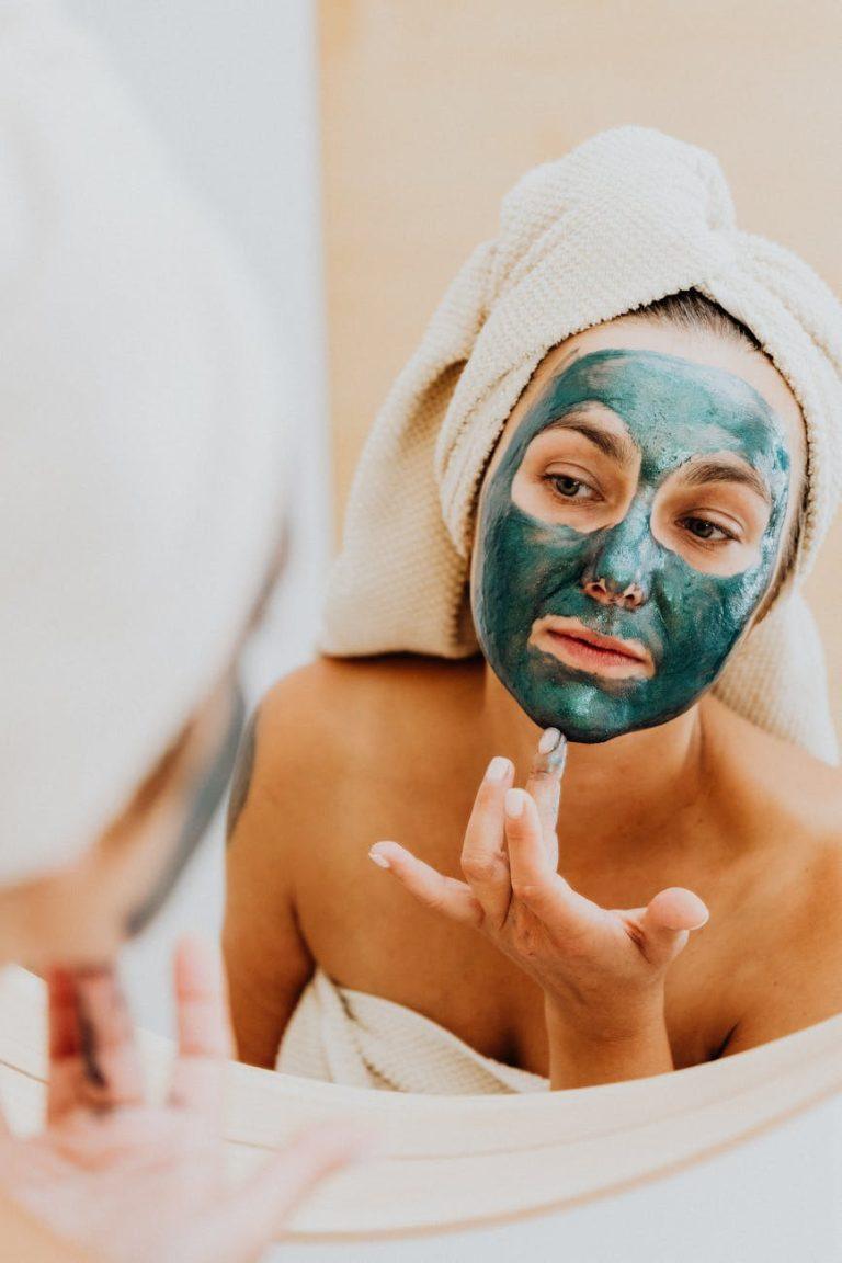 Woman applying a green DIY face mask made with avocado and herbs.